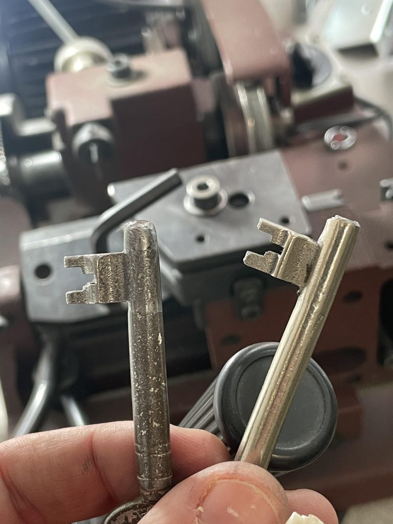 Zwei Buntbartschlüssel. Eine Kopie und ein Original vor einer Maschiene.